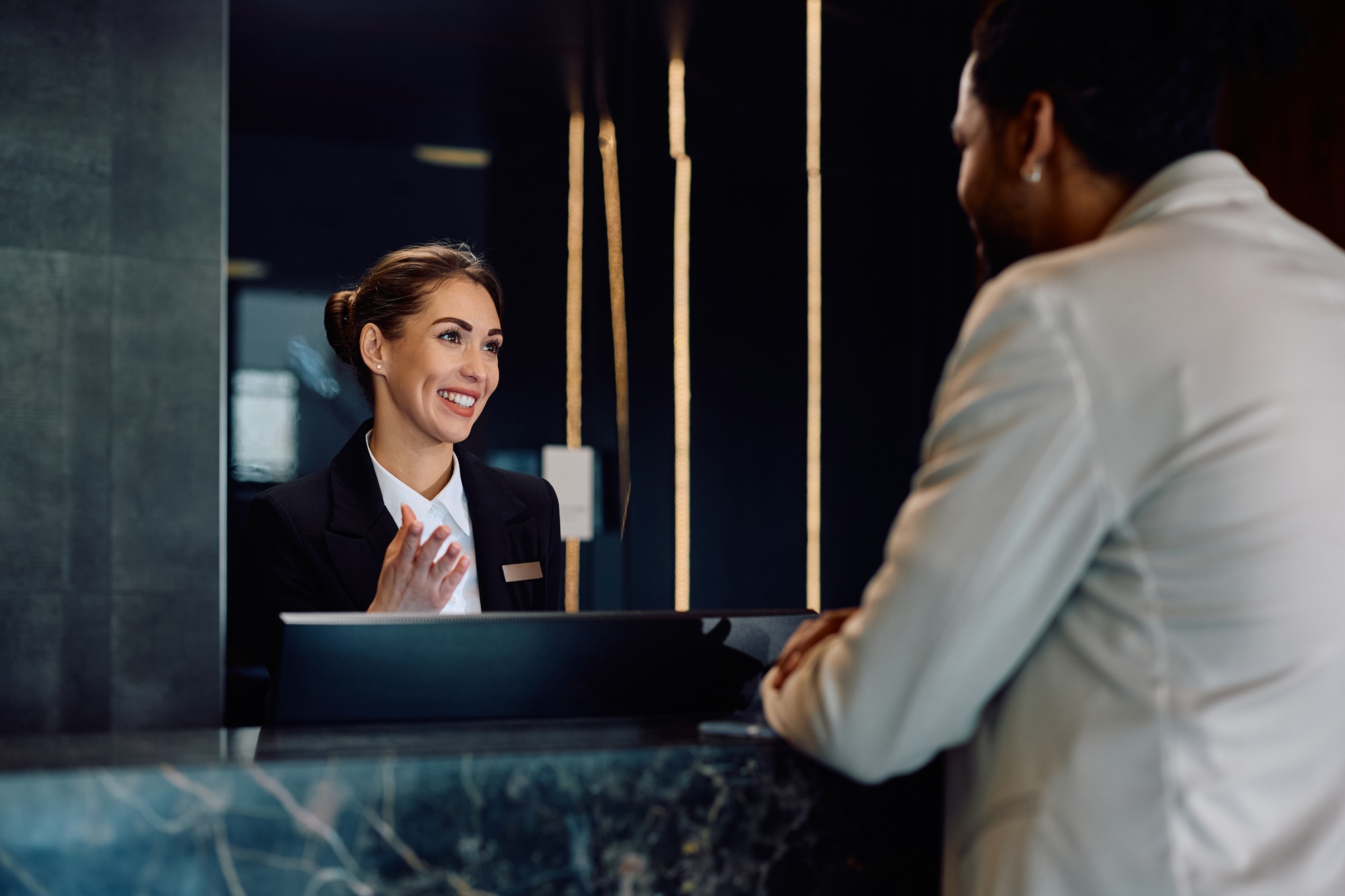 Happy hotel receptionist talking to a guest at front desk.
